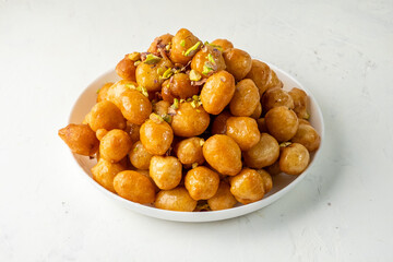 Loukoumades, luqaimat or lokma in sweet sauce made of honey covered in white plate on a light background.