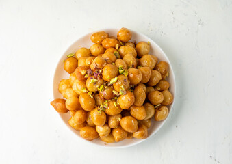luqaimat or lokma in a sweet honey sauce in a white plate on a light background, top view, free space.
