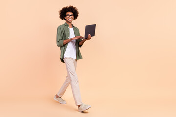 Full length body size view of attractive cheerful trendy guy going using laptop startup isolated over beige pastel color background