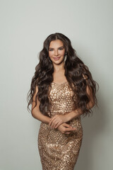 Cheerful brunette woman in luxurious gold evening gown smiling and posing on white background