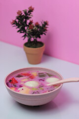 bowl of fruit soup with muesli and flowers on the pink background