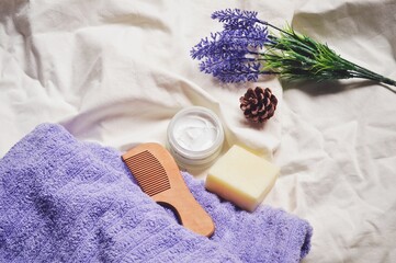 Flat lay composition photo organic beauty products for skin and hair care. Purple towel, wooden comb, moisturizing cream, solid shampoo and lavender flowers. Herbal bath products