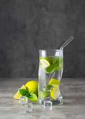 A mojito cocktail in a glass glass with a straw on a light table. Slices of lime and cubes of melted people in the background. Light background, space for text