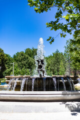 Fototapeta na wymiar Fountain. Stone fountain filled with water and surrounded by statues and buildings in a park in Madrid on a clear day with a blue sky, in Spain. Europe. Photography.