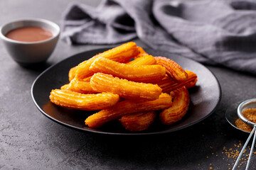 Churros dessert with chocolate sauce, topping, dip on black plate. Close up.