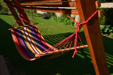 rocking chair, hammock with wooden support among the trees in the garden. view of naked hairy white legs of a rocking man, striped rainbow textile lounger with baby feet and legs tangled in cloth