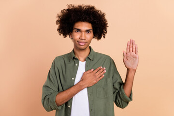 Portrait of attractive sincere wavy-haired guy touching heart promise isolated over beige pastel...