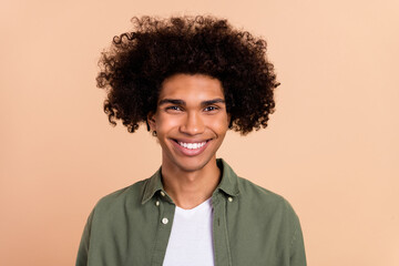 Fototapeta na wymiar Portrait of attractive funky cheerful wavy-haired guy with chevelure wearing green shirt isolated over beige pastel color background
