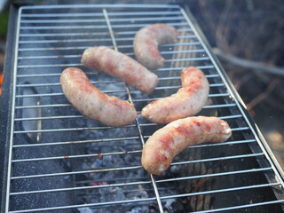 Grilled sausages on grill with smoke and flame on a meadow. Barbecue picnic.
