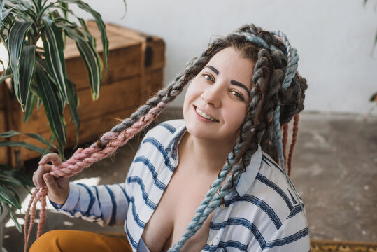 Closeup Portrait of positive smiling plus size woman with dreadlocks  sitting on the floor and hold her hair in bohemian boho interior 