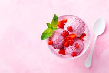 Ice cream sundae with strawberry in a glass bowl on pink background. Copy space. Top view.