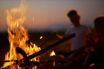 Sparkling bonfire, with blurred tourists sitting around in summer night. Close up view of campfire...