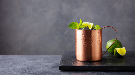 Moscow mule cocktail in copper mug with fresh mint, lime on marble board. Grey background. Copy...