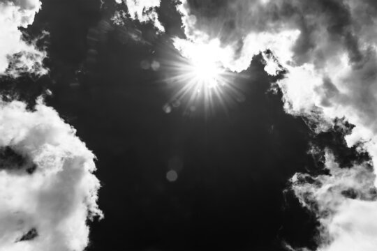 a heavenly landscape with a bright sun breaking through the clouds in a blue sky, black and white photo