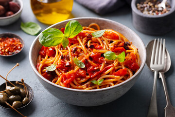 Pasta, spaghetti with tomato sauce, olives and fresh basil. Puttanesca recipe. Grey background....