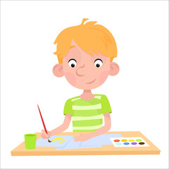 A boy with blond hair sits at a table and draws with a brush and paints