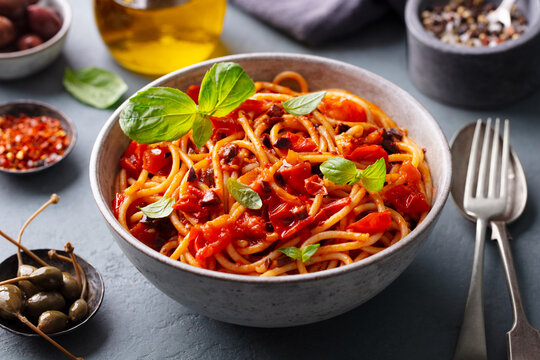Pasta, spaghetti with tomato sauce, olives and fresh basil. Puttanesca recipe. Grey background. Close up.