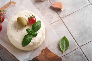 Ricotta cheese. Homemade Ricotta cheese with basil, garlic, tomatoes and green olives on parchment paperback and stand on old beige tiles background. Italian food.  Selective focus.