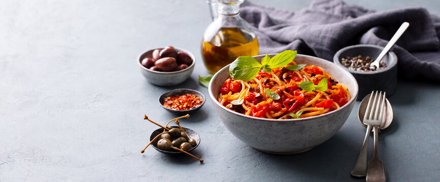 Pasta, spaghetti with tomato sauce, olives and fresh basil. Puttanesca recipe. Grey background. Copy space.