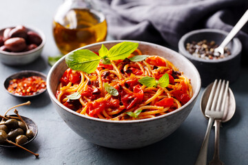 Pasta, spaghetti with tomato sauce, olives and fresh basil. Puttanesca recipe. Grey background. Close up.