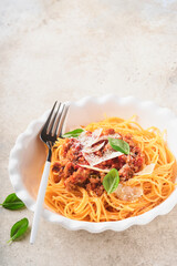 Pasta spaghetti Bolognese. Tasty appetizing italian spaghetti with bolognese sauce, tomato sauce, cheese parmesan and basil on white plate on grey stone or concrete table background. Top view.