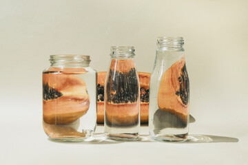 Fresh juicy halved papaya on beige background, behind glass bottles with water. Optical illusion, creative composition.