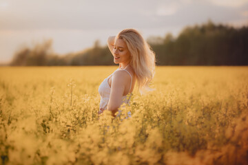 Uśmiechnięta dziewczyna w białej sukience na polu żółtych kwiatów - obrazy, fototapety, plakaty