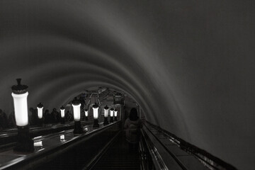 Descending the escalator in the city subway. A dark tunnel. Lanterns going off into the distance.