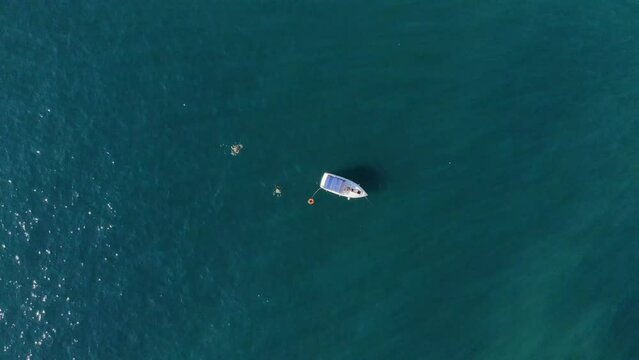 A ship with tourists is anchored in a bay of the Mediterranean Sea with people swimming nearby. aerial view