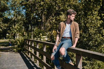 Fototapeta premium Boy sitting on the railing of a bridge looking at the river that crosses