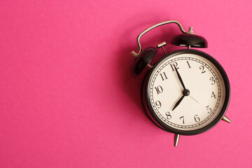 black vintage style alarm clock isolated on a pink background