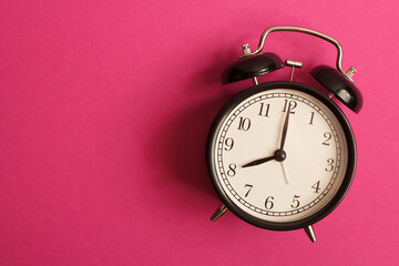 black vintage style alarm clock isolated on a pink background