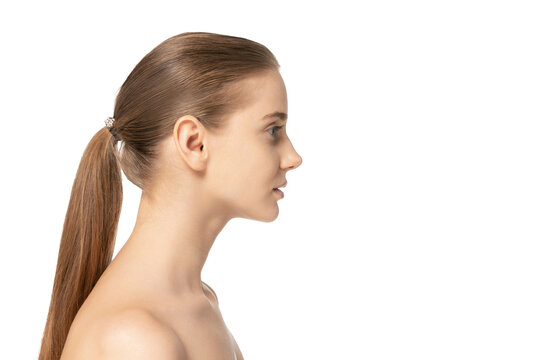 Side view portrait of young beautiful girl with low ponytail posing isolated over white studio background. Clear face