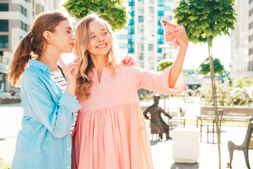 Two young beautiful smiling hipster female in trendy summer dresses.Sexy carefree women posing in the street. Positive pure models having fun at sunset, hugging and going crazy. Taking selfie