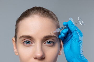 Cropped portrait of young girl doing cosmetology injections isolated over grey studio background. Removing wrinkles