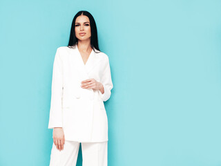 High fashion portrait of young beautiful brunette woman wearing nice trendy white suit. Sexy fashion model posing in studio. Fashionable female isolated on blue