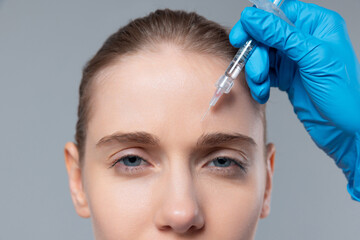 Cropped portrait of young girl doing cosmetology injections isolated over grey background. Removing wrinkles on forehead. Botox treatment