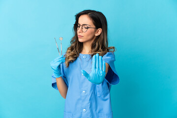 Woman dentist holding tools over isolated on blue background making stop gesture and disappointed