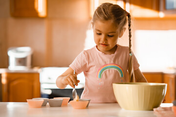 Cute smiling little blonde girl cooking dough in kitchen at home