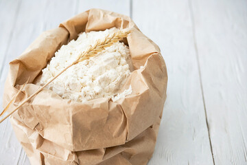 Wheat flour in paper pack with ears of wheats on white wooden table.