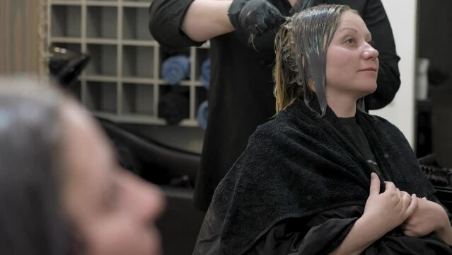Hairdresser dyes the gray hair of a smiling woman. Hair coloring in a beauty salon