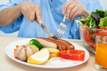 Asian senior or elderly old lady woman patient eating breakfast and vegetable healthy food with hope and happy while sitting and hungry on bed in hospital.