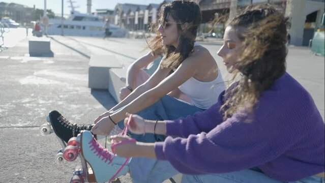 Slomo side view of three girls tying rollerskates on sunny windy day