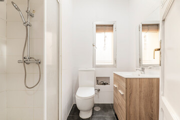 Bathroom with wooden furniture, frameless square mirror, porcelain sink, shower cabin with chrome accessories, translucent glass window and white painted solid wood door
