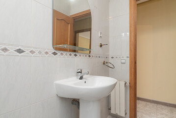 Fototapeta na wymiar Bathroom with mirror with glass shelf, porcelain sink with foot of the same material, small white aluminum radiator and exit to a corridor