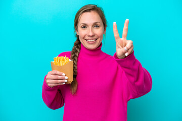 Young caucasian woman holding fried chips isolated on blue background smiling and showing victory sign