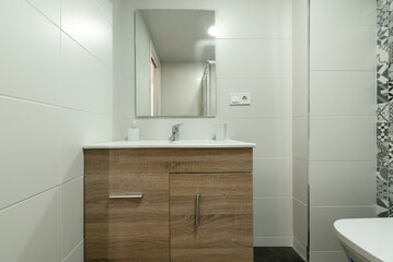 Bathroom with wooden cabinet with white porcelain sink and light gray tiles