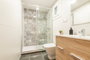 Bathroom with wooden cabinet with drawers, white porcelain sink, square frameless mirror, glass shower stall and white tiles