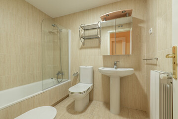 Bathroom with cabinet doors with mirror, porcelain sink with the same material, bathtub with glass screen and ceramic tiles