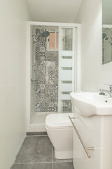 toilet with white wooden bathroom cabinet with frameless mirror, shower cabin with screen and wall tiled with hydraulic tiles